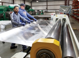 professional fabrication services with workers rolling metal anodized sheet in a factory